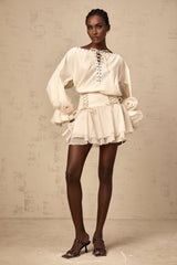 A woman wearing a matching two piece outfit consisting of a ruffled blouse with self tie straps and a coordinating skirt both in a light fabric