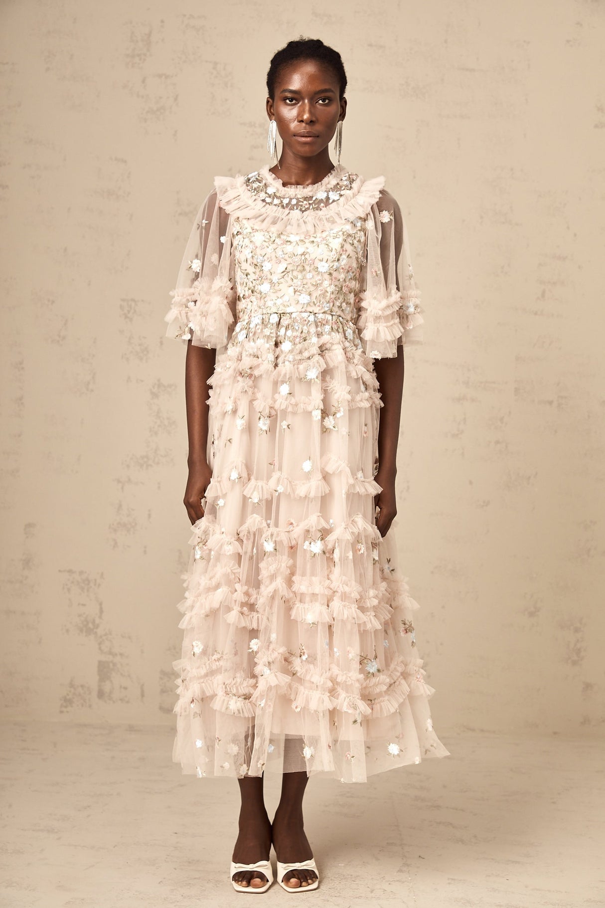 A woman wearing a midi dress with floral embroidery and tiered ruffles