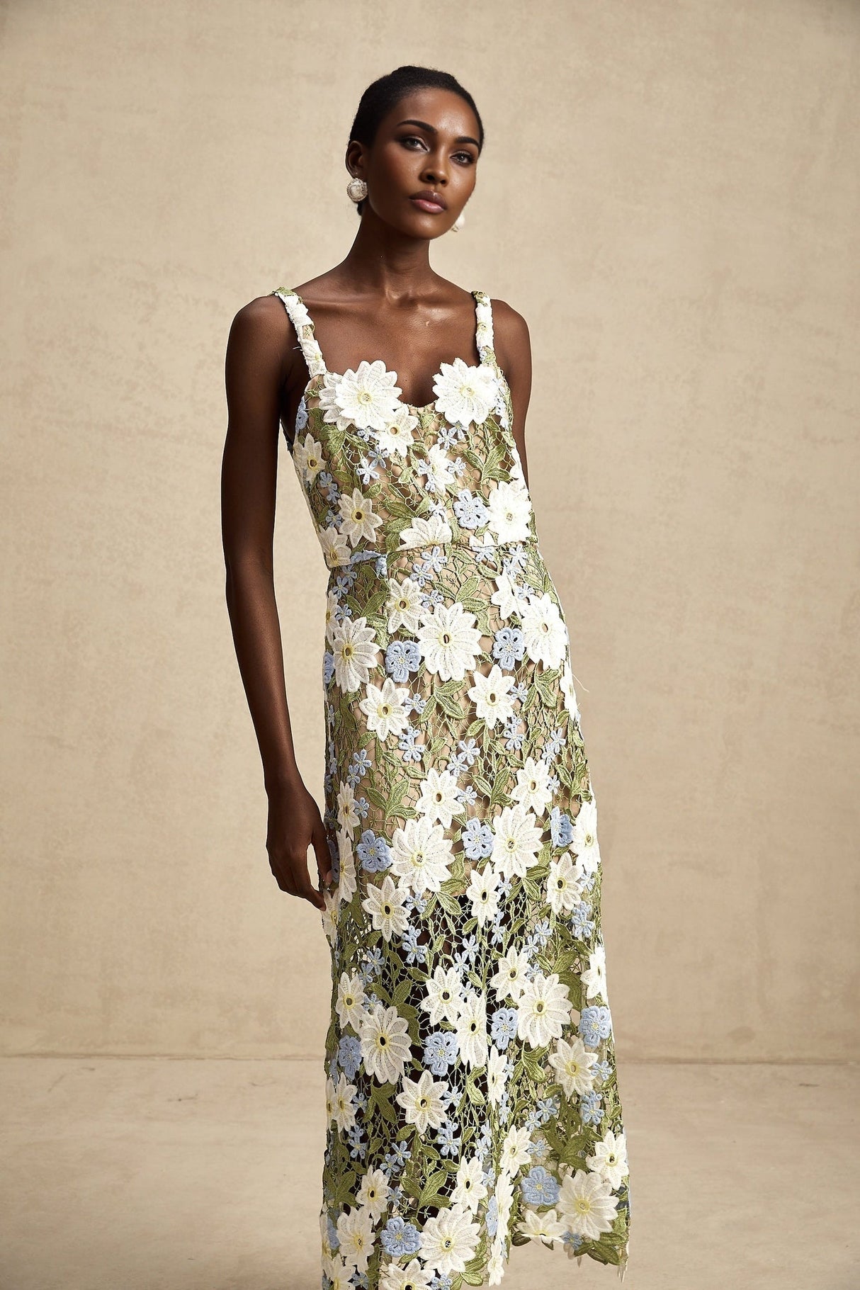 A woman wearing a midi length dress with floral embroidery and cutout details The dress features a fitted bodice and flowing skirt in a light colored fabric