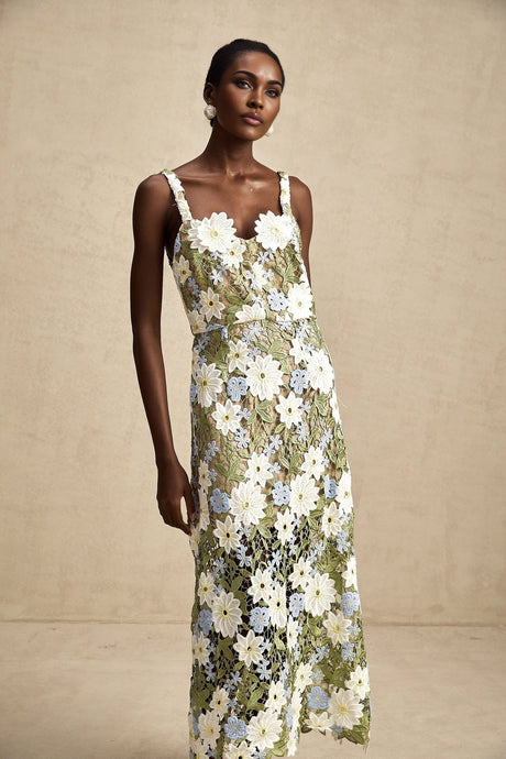 A woman wearing a midi length dress with floral embroidery and cutout details The dress features a fitted bodice and flowing skirt in a light colored fabric