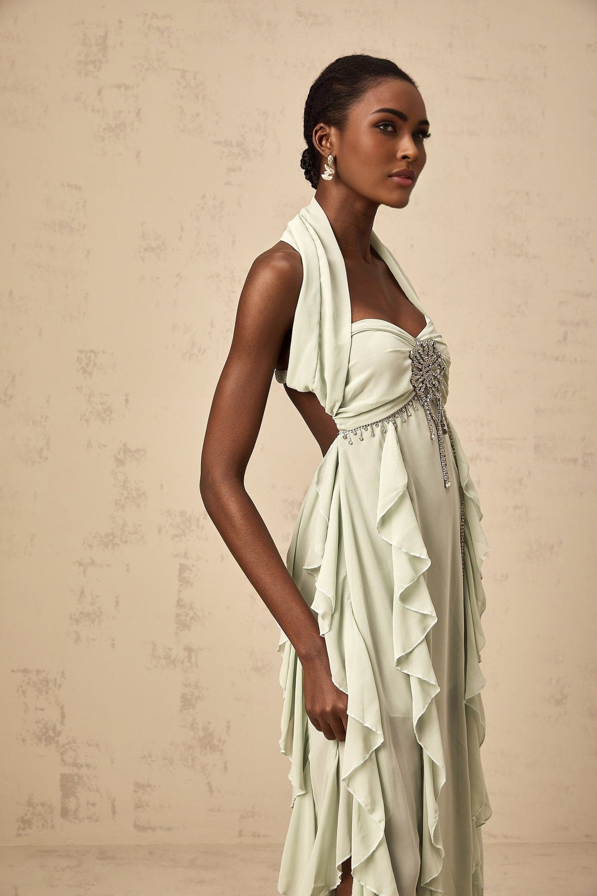 A woman wearing a midi length dress with ruffled details and embellishments standing in a neutral pose