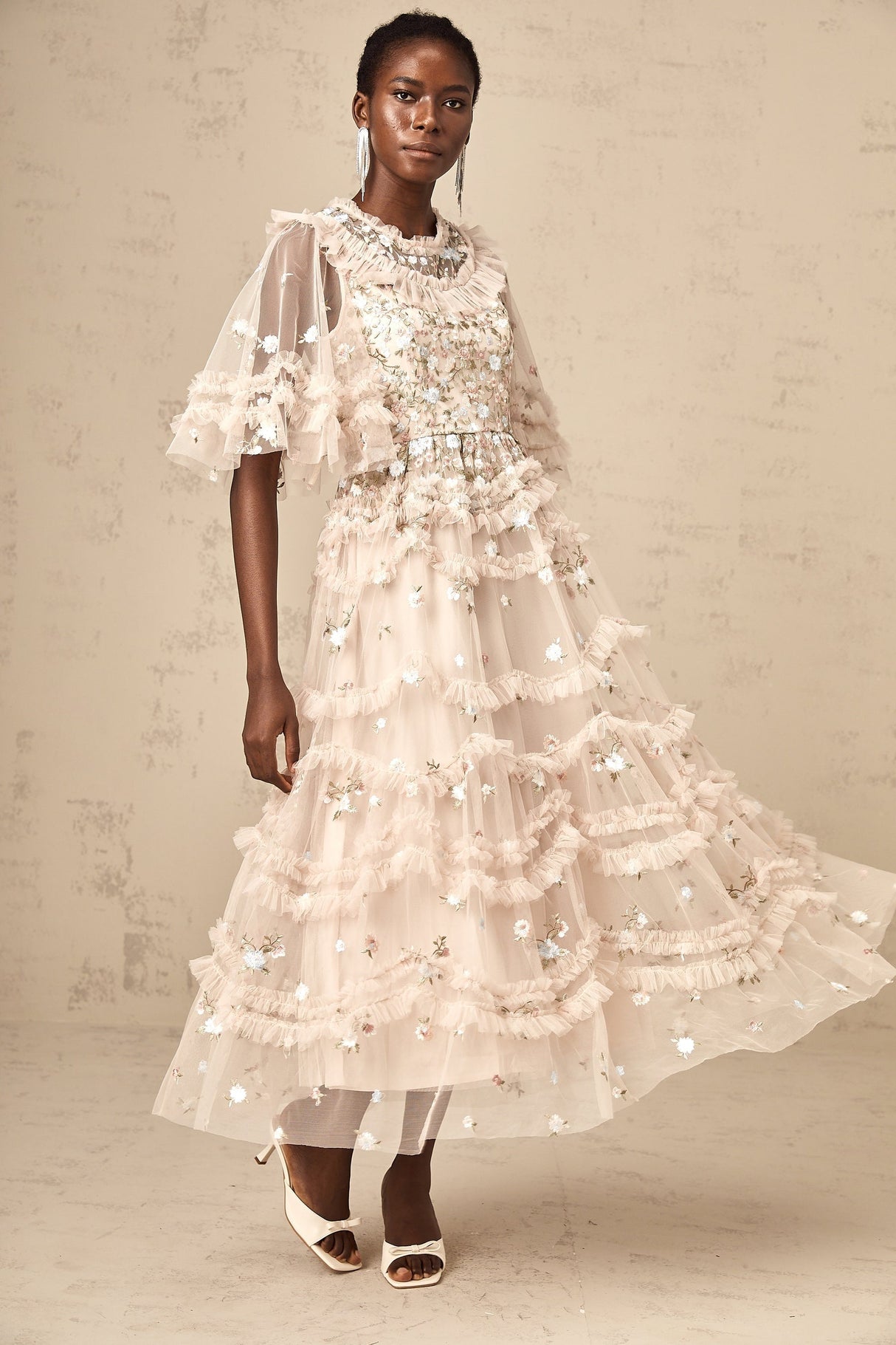 A woman wearing a midi length dress with tiered ruffles and floral embroidery design standing in a relaxed pose