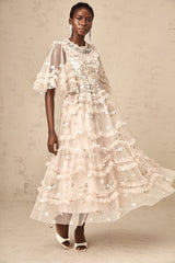 A woman wearing a midi length dress with tiered ruffles and floral embroidery design standing in a relaxed pose