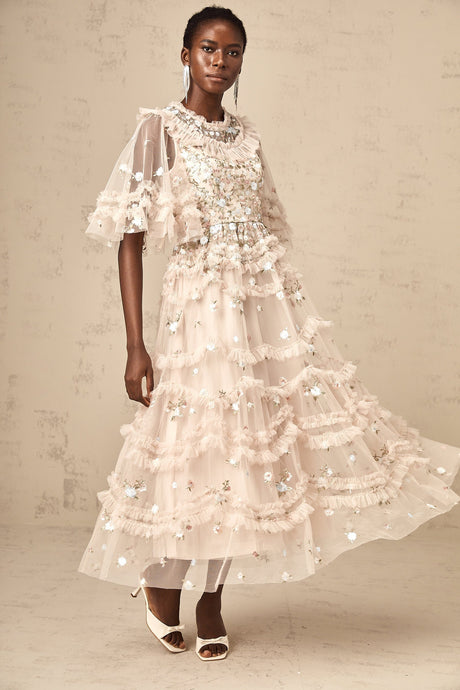 A woman wearing a midi length dress with tiered ruffles and floral embroidery design standing in a relaxed pose