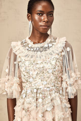 A woman wearing a midi length dress with tiered ruffles and floral embroidery details The dress has a delicate feminine design with a fitted bodice and flowing skirt