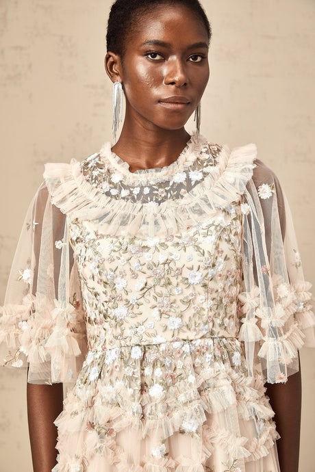 A woman wearing a midi length dress with tiered ruffles and floral embroidery details The dress has a delicate feminine design with a fitted bodice and flowing skirt