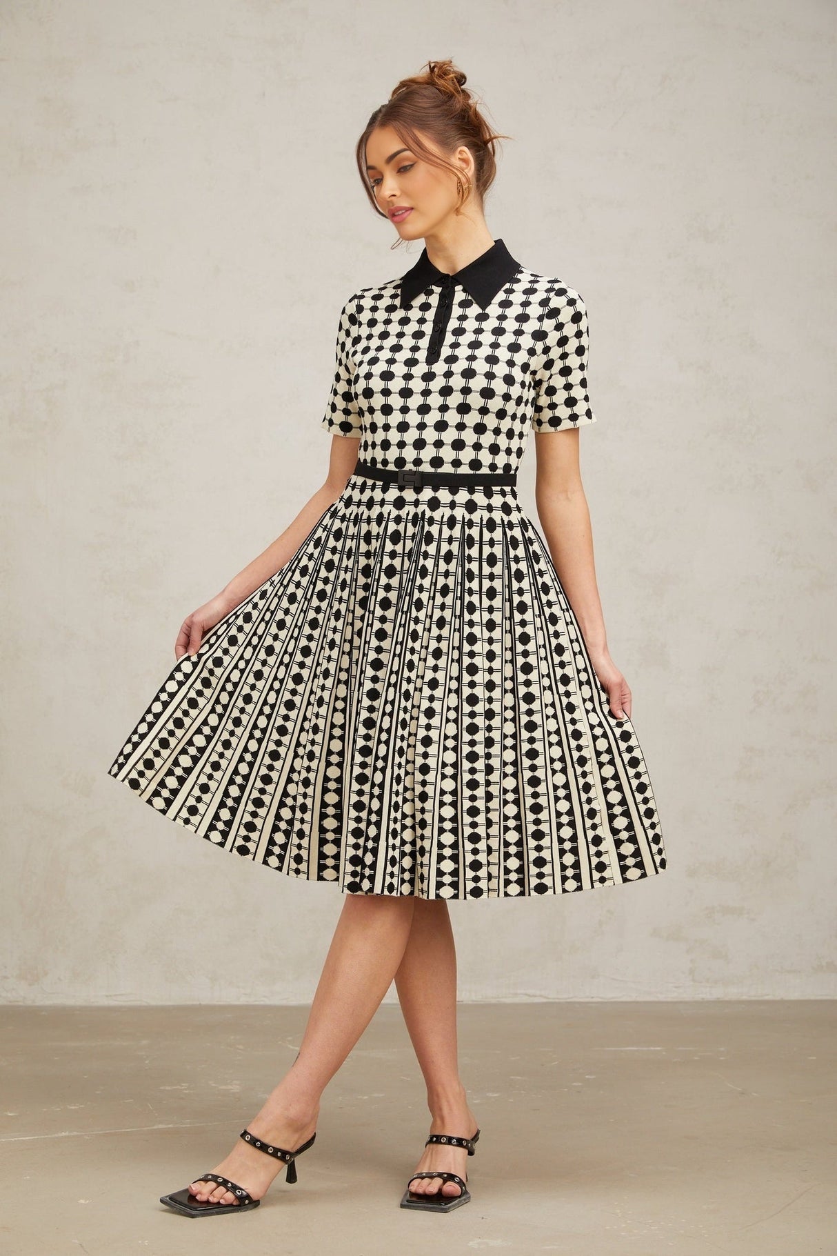 A woman wearing a midi length knit dress with color blocked sections and polka dot patterns in contrasting colors