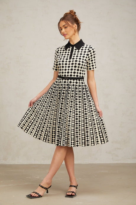 A woman wearing a midi length knit dress with color blocked sections and polka dot patterns in contrasting colors