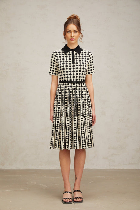 A woman wearing a midi length knit dress with color blocked sections and polka dot patterns in contrasting colors