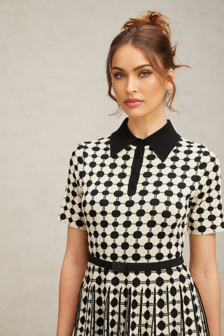 A woman wearing a midi length knit dress with color blocked sections and polka dot patterns in contrasting colors