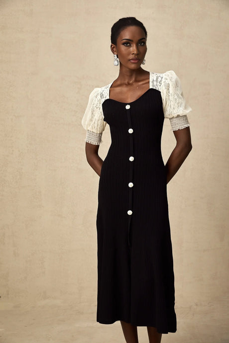 A woman wearing a midi length knit dress with lace trim details along the neckline and hem standing in a neutral pose against a plain background