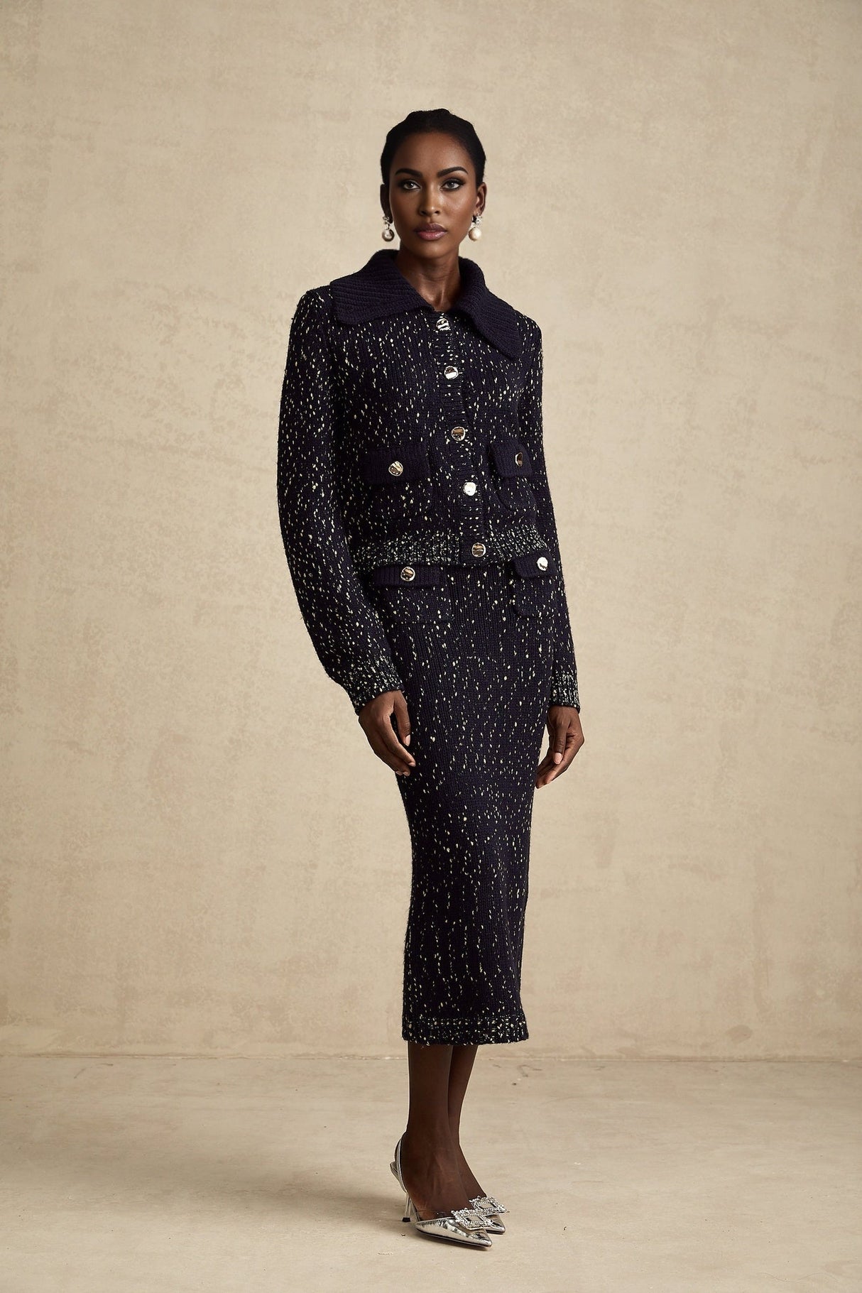 A woman wearing a navy blue crochet knit jacket and matching skirt set standing against a plain background