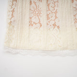 A woman wearing a neutral colored mini dress with floral lace pattern and flared cuffs standing in a relaxed pose