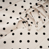 A woman wearing a neutral colored mini dress with polka dots and puff sleeves standing in a relaxed pose