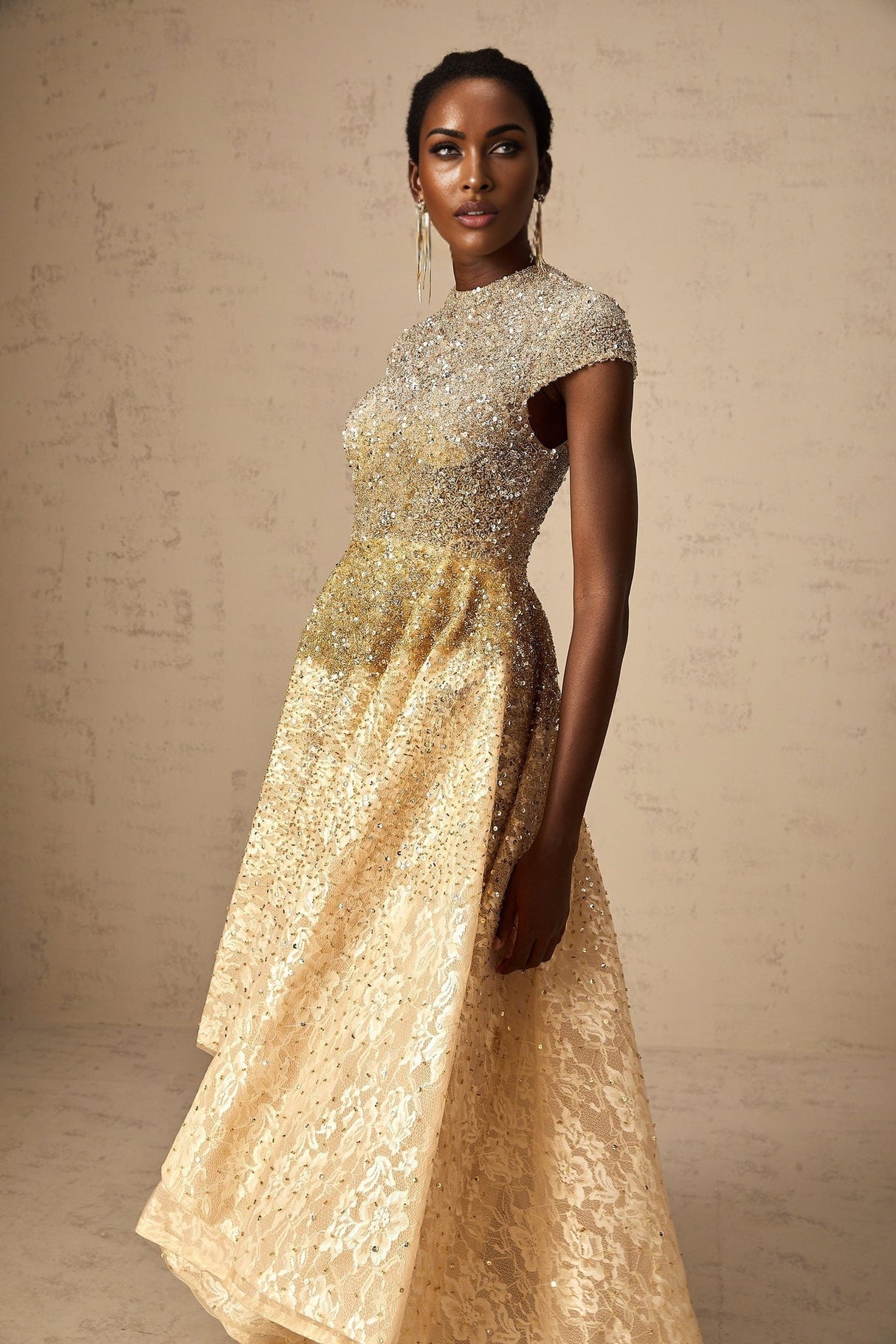 A woman wearing a neutral colored sequined dress with a high low hemline standing in a relaxed pose