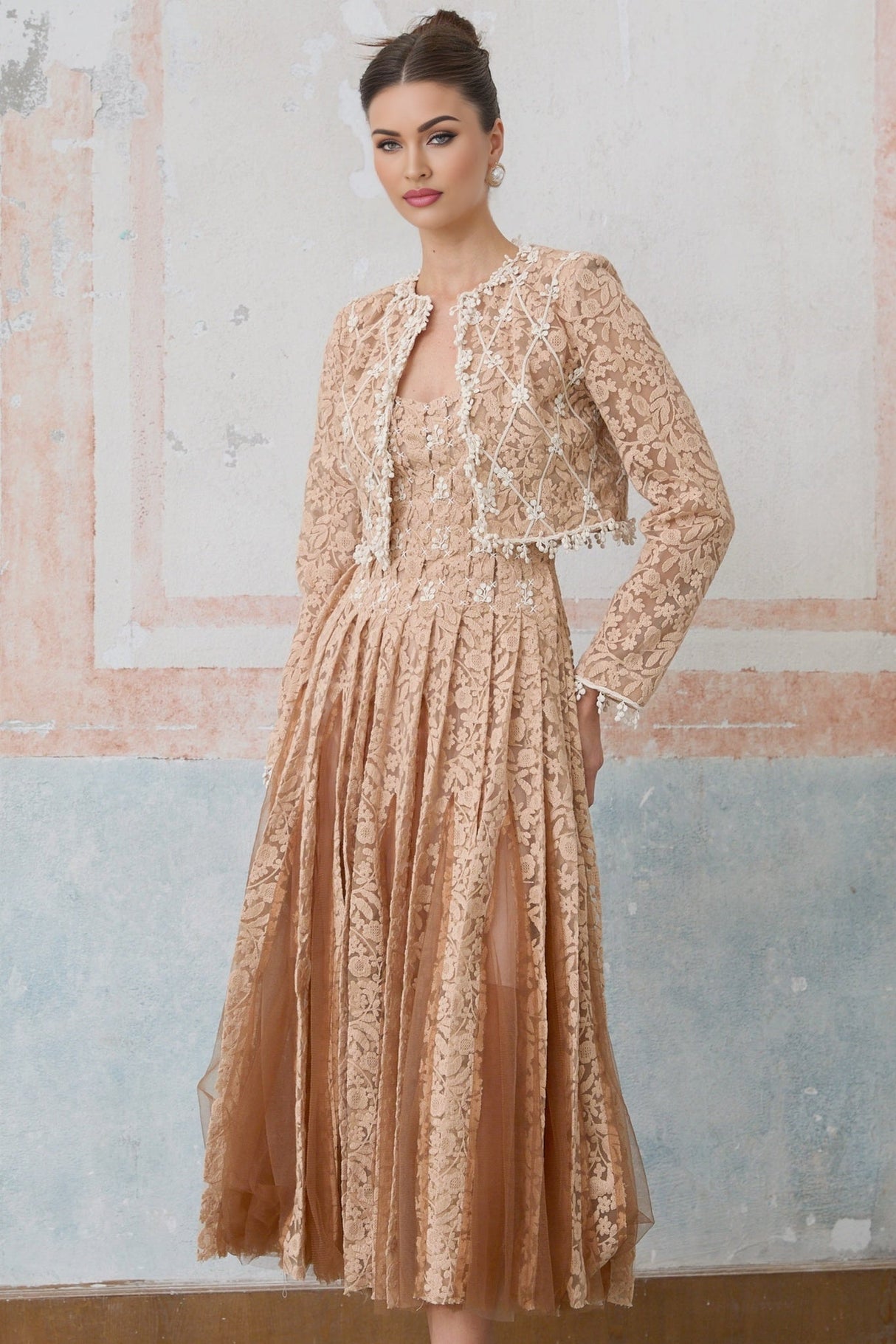A woman wearing a neutralcolored crochetlace cardigan over a matching dress standing in a relaxed pose against a plain background