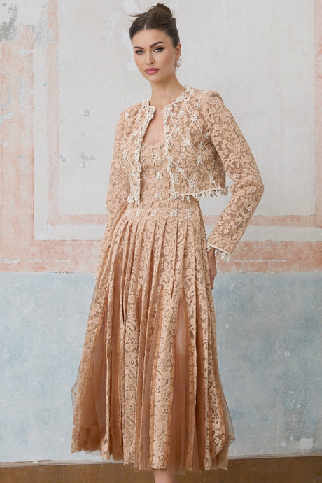 A woman wearing a neutralcolored crochetlace cardigan over a matching dress standing in a relaxed pose against a plain background