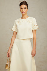 A woman wearing a neutralcolored matching set consisting of a top and skirt The top features delicate 3D petal details and the skirt has a fitted silhouette Both pieces are in soft beige tones creating an elegant and feminine ensemble