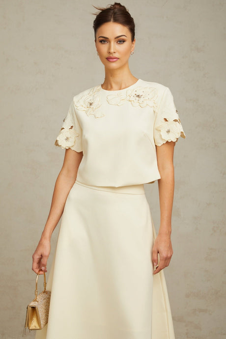 A woman wearing a neutralcolored matching set consisting of a top and skirt The top features delicate 3D petal details and the skirt has a fitted silhouette Both pieces are in soft beige tones creating an elegant and feminine ensemble