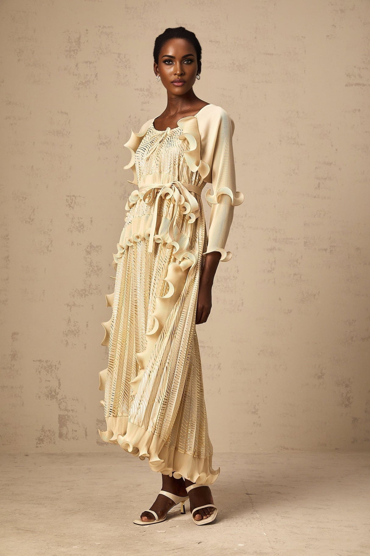 A woman wearing a neutralcolored midi dress with gilded ruffles and a fitted silhouette standing in a relaxed pose