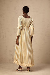 A woman wearing a neutralcolored midi dress with gilded ruffles and delicate details standing in a relaxed pose