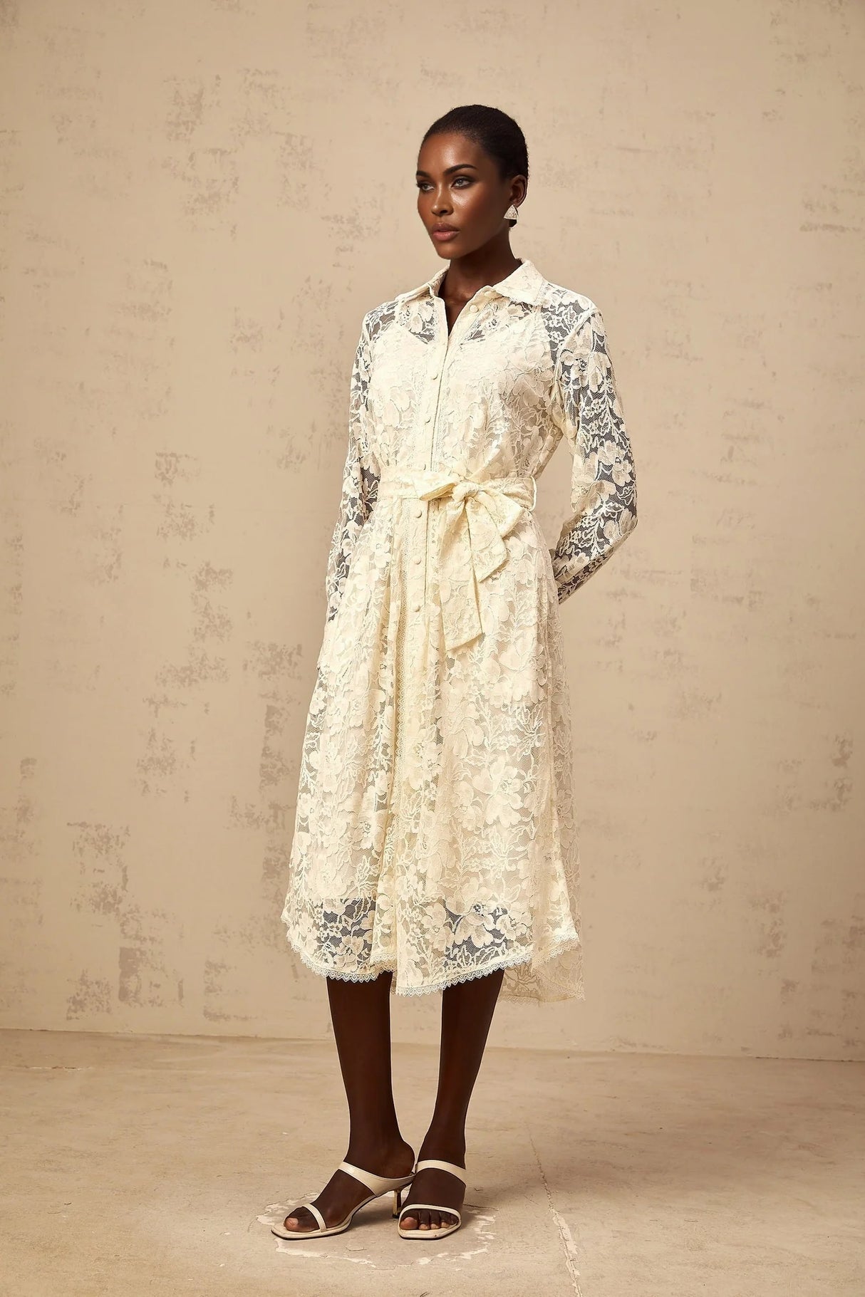 A woman wearing a neutralcolored midi shirt dress with delicate guipure lace detailing standing in a relaxed pose against a plain background