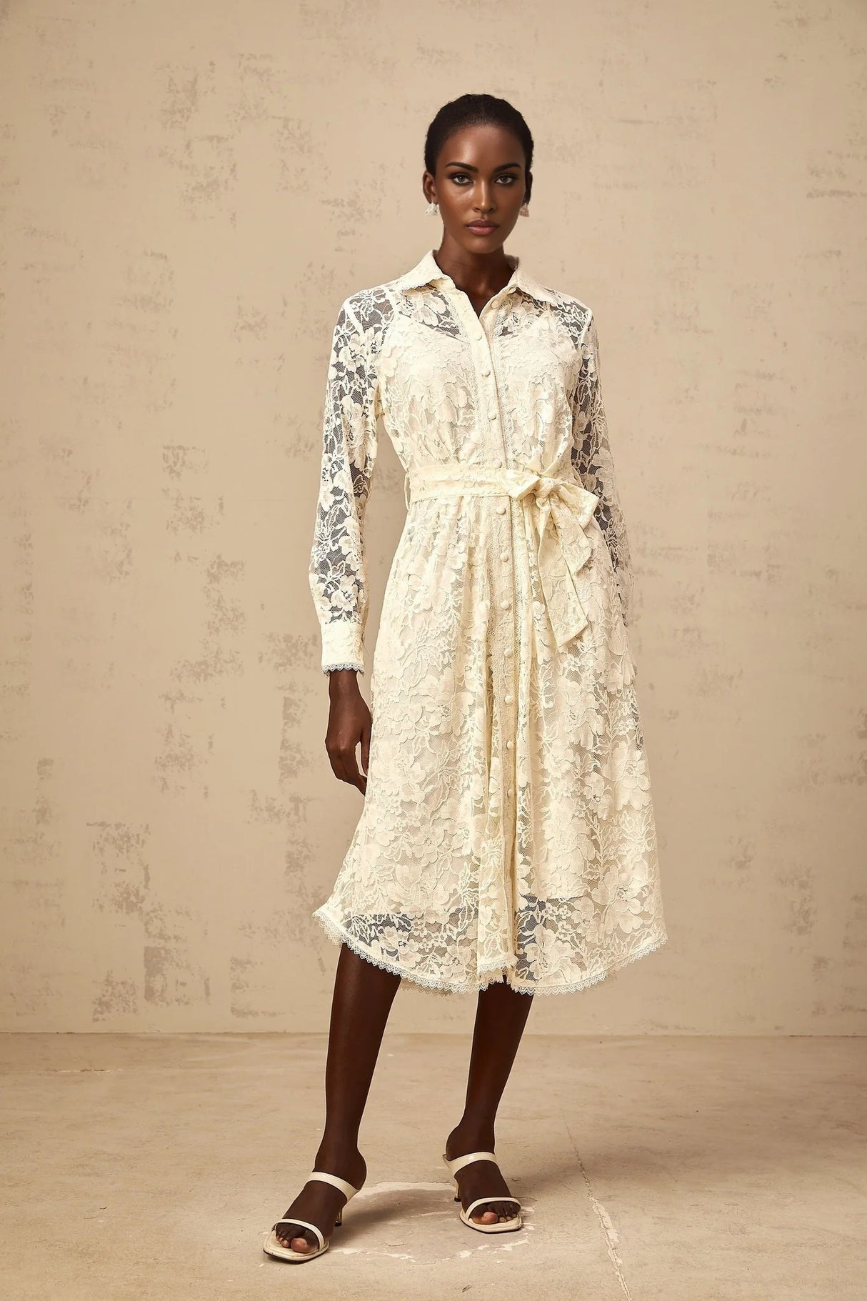 A woman wearing a neutralcolored midi shirt dress with guipure lace detailing standing in a casual pose
