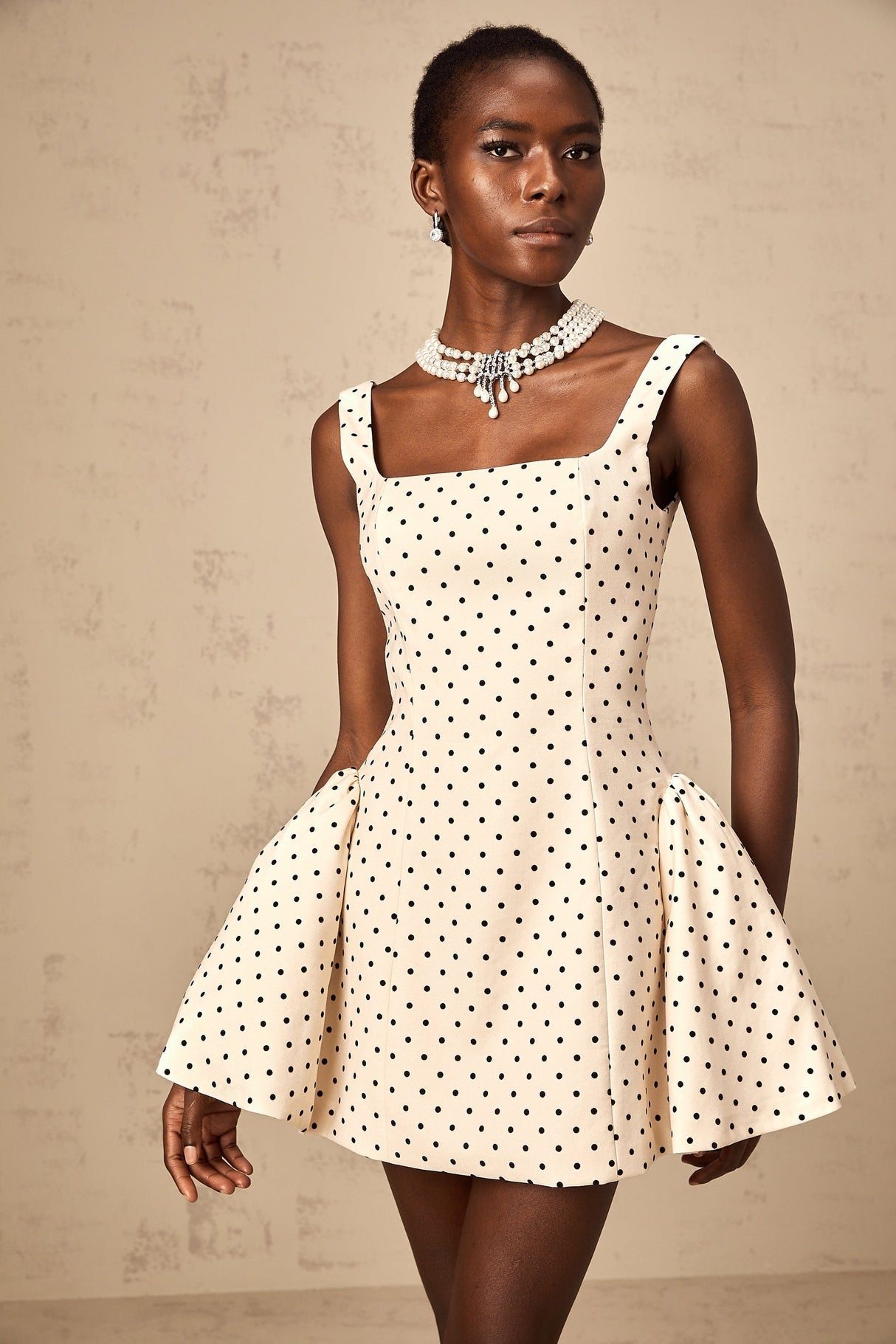 A woman wearing a neutralcolored mini dress with polka dots and puff sleeves standing in a casual pose