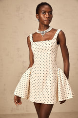 A woman wearing a neutralcolored mini dress with polka dots and puff sleeves standing in a casual pose