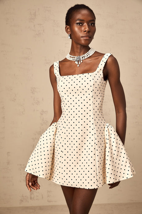 A woman wearing a neutralcolored mini dress with polka dots and puff sleeves standing in a casual pose