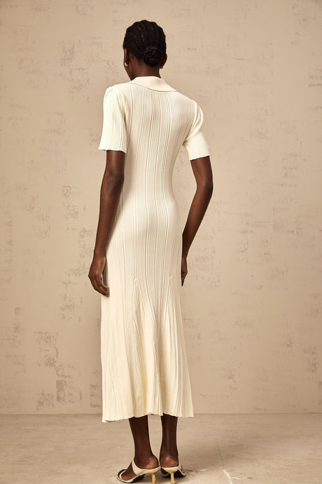 A woman wearing a neutralcolored ribbed knit midi dress with a formfitting silhouette standing against a plain background