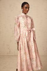A woman wearing a pink midi dress with floral print and embellishments standing against a plain background