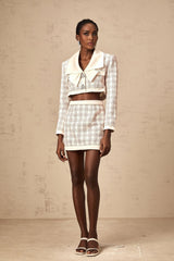 A woman wearing a pink tweed jacket and matching skirt with a checkered pattern standing against a plain background