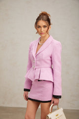 A woman wearing a pink tweed matching set consisting of a sleeveless top and mini skirt The outfit has a textured fabric with a classic tweed pattern
