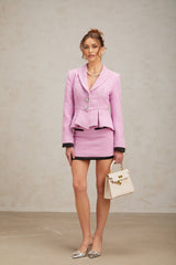 A woman wearing a pink tweed matching set consisting of a sleeveless top and mini skirt The outfit has a textured fabric with a subtle pattern and a classic feminine style