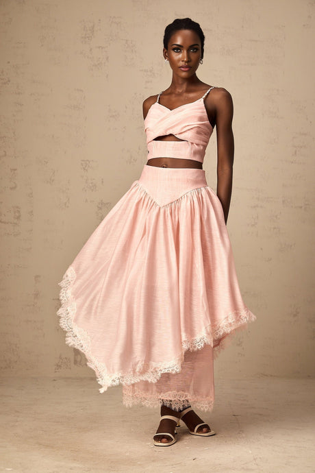 A woman wearing a pink twopiece outfit consisting of an asymmetric ruffled top and matching skirt set