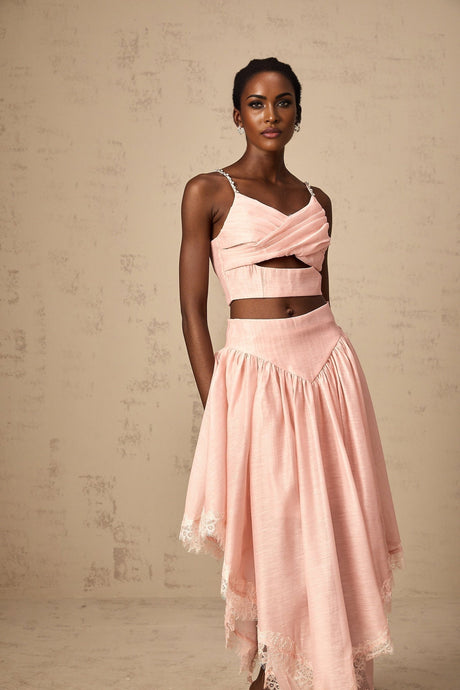 A woman wearing a pink twopiece outfit consisting of an asymmetric ruffled top and matching skirt