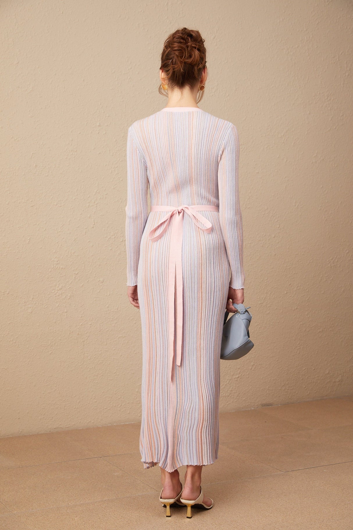 A woman wearing a pleated knit midi dress with a V neckline in a soft color standing against a plain background