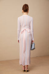 A woman wearing a pleated knit midi dress with a V neckline in a soft color standing against a plain background