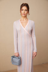 A woman wearing a pleated knit midi dress with a V neckline The dress has long sleeves and falls to mid calf length The fabric appears soft and textured with vertical pleats throughout
