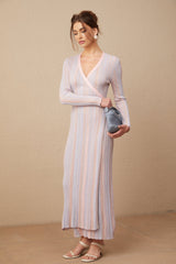 A woman wearing a pleated knit midi dress with a Vneck in a soft color standing against a neutral background