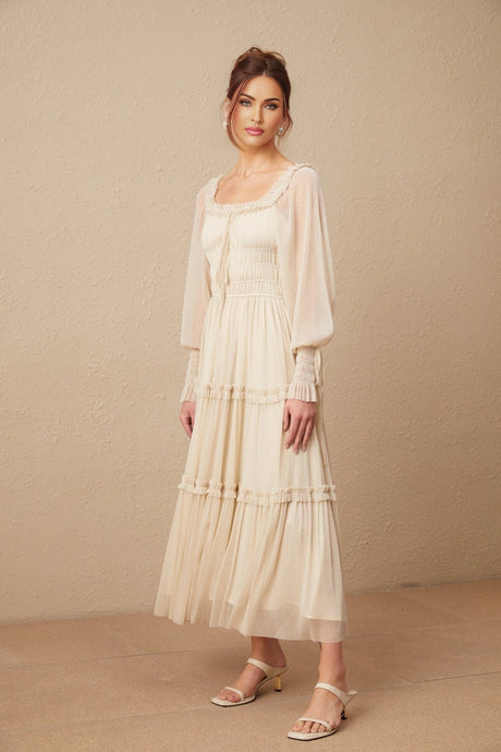 A woman wearing a pleated metallic midi dress with shirred detailing and a flowy skirt standing in an elegant pose