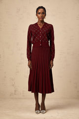 A woman wearing a red argyle knit cardigan and matching skirt set with embellishments The cardigan features an intarsia knit pattern and the outfit is styled as a coordinated ensemble