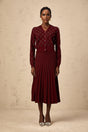 A woman wearing a red argyle knit cardigan and matching skirt set with embellishments The cardigan features an intarsia knit pattern and the outfit is styled as a coordinated ensemble