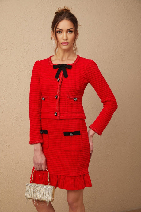 A woman wearing a red braided waffle knit jacket and matching skirt set The jacket has a textured pattern and the skirt is short and form fitting The outfit is styled as a coordinated two piece ensemble