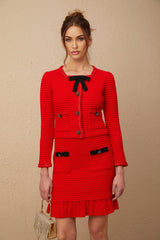 A woman wearing a red braided waffle knit jacket paired with a matching skirt forming a coordinated outfit set
