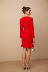 A woman wearing a red braided waffle knit jacket paired with a matching skirt standing against a plain background