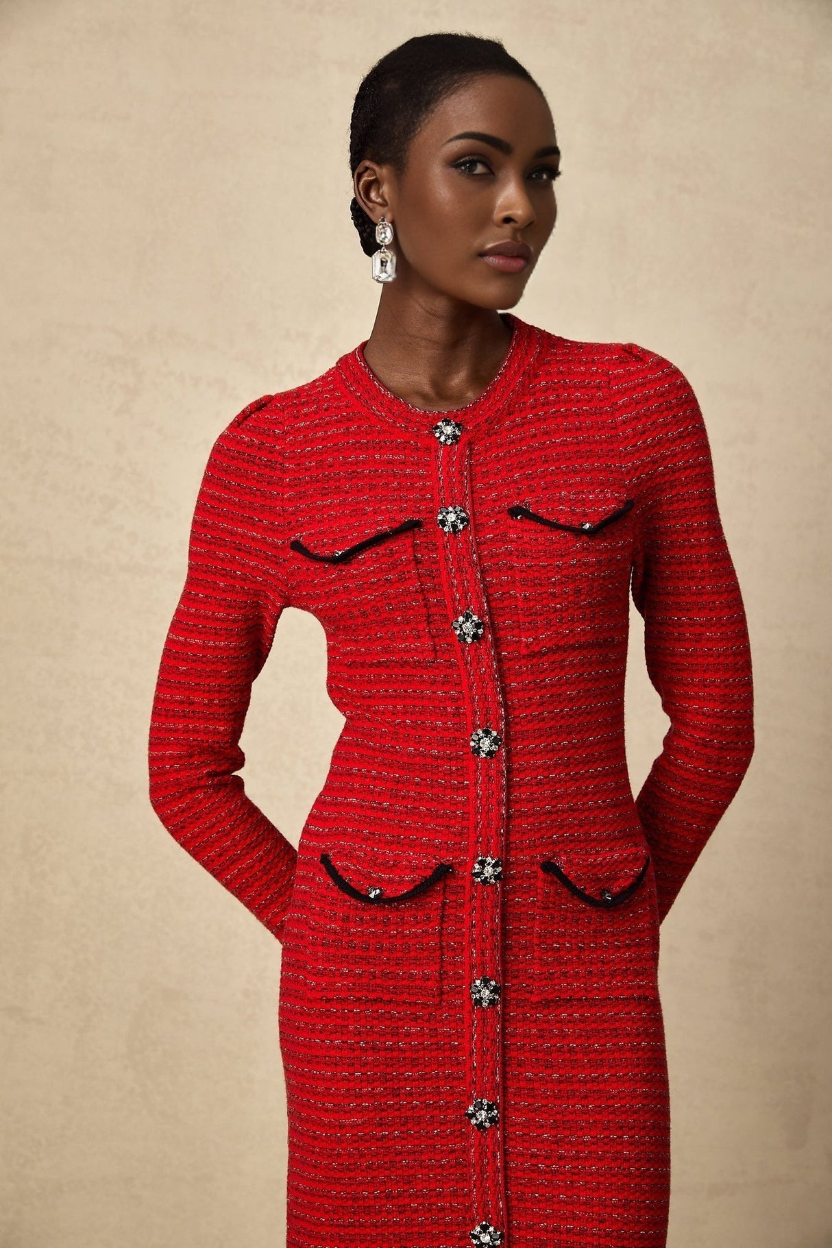 A woman wearing a red knitted midi dress with embellishments standing in a relaxed pose