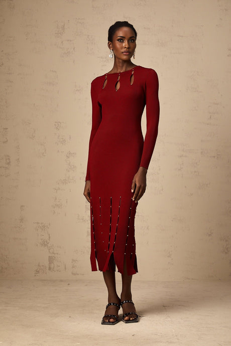 A woman wearing a red knitted midi dress with long sleeves and beaded details The dress features cutout sections and falls to mid calf length