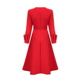A woman wearing a red long sleeve dress with floral patterns standing in a neutral background